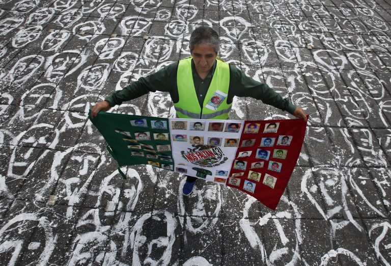 AP Photo,ARCHIVO - En esta foto de archivo del 26 de septiembre de 2016, un hombre en Ciudad de México carga una bandera mexicana que tiene los retratos de los 43 estudiantes desaparecidos de la escuela normal rural de Ayotzinapa, en el estado de Guerrero. (AP Foto/Marco Ugarte, Archivo)
