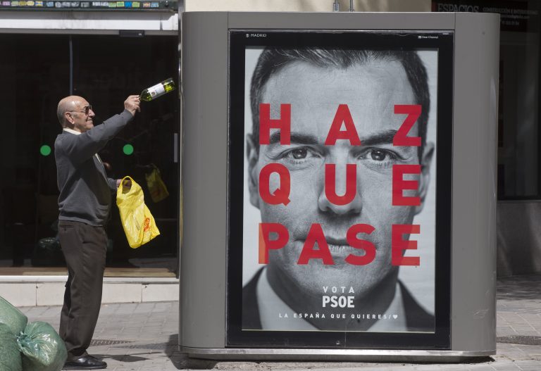 AP Photo,Un hombre tira una botella vacía en un contenedor de reciclaje con un poster electoral con el rostro del presidente Pedro Sánchez en Madrid, España, el martes 16 de abril de 2019. (AP Foto/Paul White)